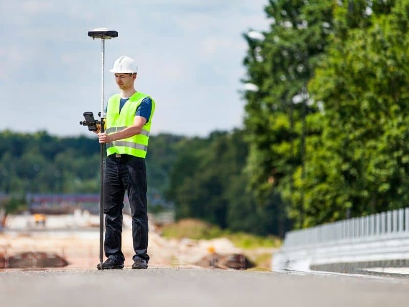 Land surveying professional using GPS equipment to measure property boundaries near a roadway