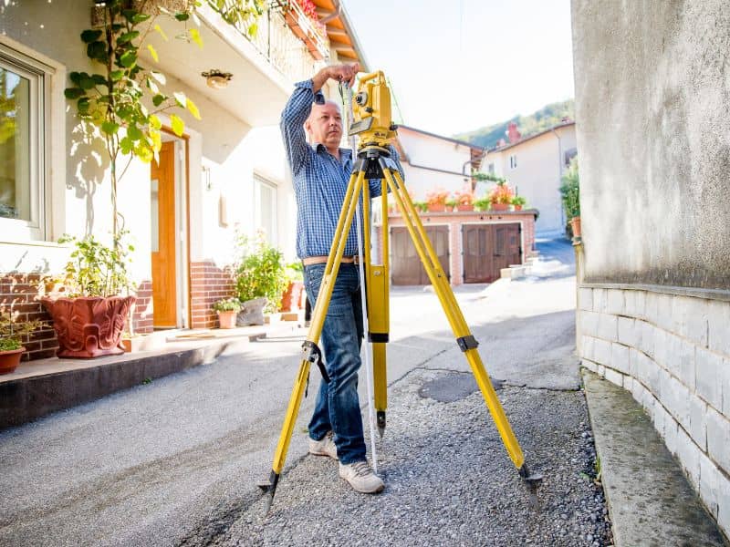 Surveyor measuring elevations near a home to prepare updated elevation certificate information